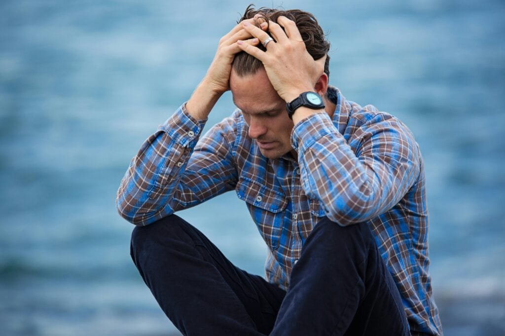 A young man holding his head with both hands to show anxiety and worry.