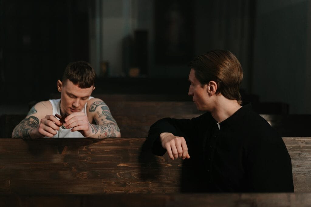 A priest with a man with multiple tattoes